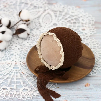 Cute brown knit baby hat with lace trim on a wooden plate, perfect for newborn photography props and costumes.