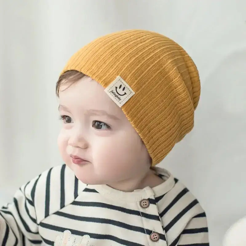 Baby wearing a soft yellow knitted hat with a smiley patch, perfect for boys and girls in all seasons.