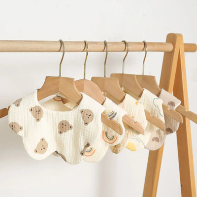 Newborn baby bibs and burp cloths hanging on a wooden rack, featuring cute bear and rainbow patterns.