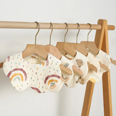 Newborn baby bibs in rainbow patterns hanging on wooden hangers, perfect for feeding and drooling.