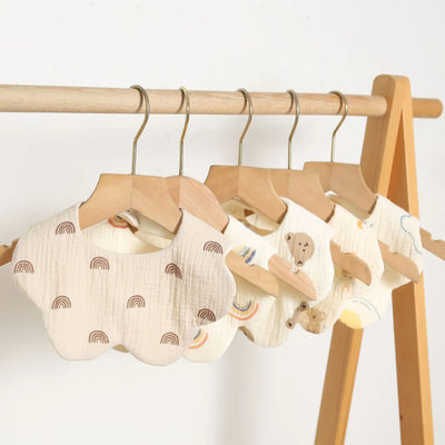 Hanging newborn baby bibs with rainbow patterns and animal designs on a wooden rack, perfect for feeding and drooling.