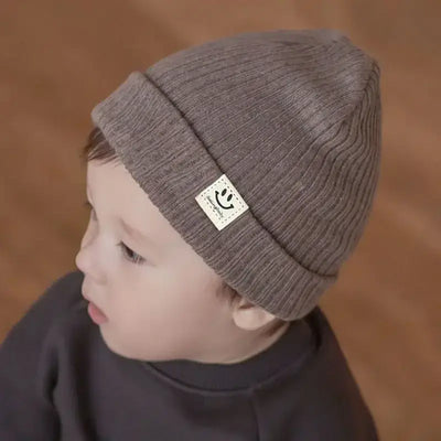 Toddler wearing a cozy brown knitted beanie with a smiley label, perfect for winter and all seasons.