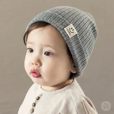 Adorable baby wearing a soft gray knitted beanie, perfect for winter, featuring a smiley face tag.